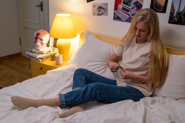 Сидящая на постели девушка рассматривает презерватив